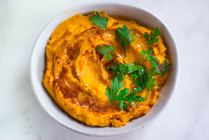 Overhead image of Healthy Sweet Potato Hummus in a serving bowl. The sweet potato hummus is garnished with parsley, paprika, and olive oil.