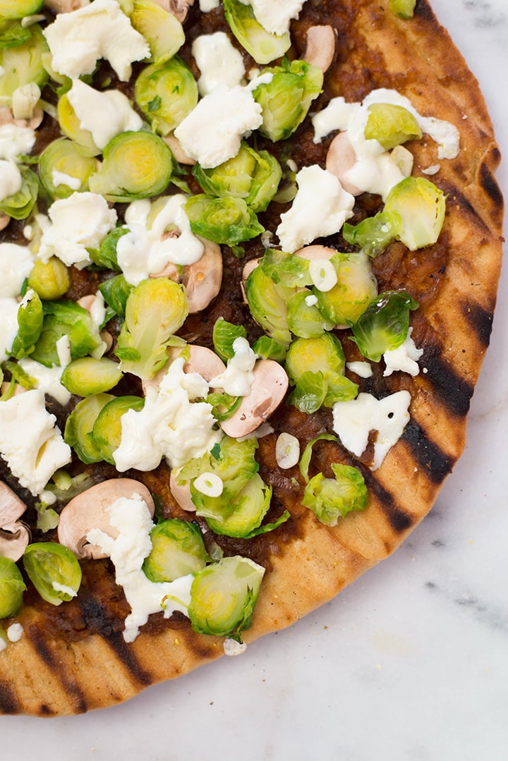 Closeup overhead image of freshly made Grilled Pizza with Maple Onion Jam, topped with shaved Brussel Sprouts and mushrooms.
