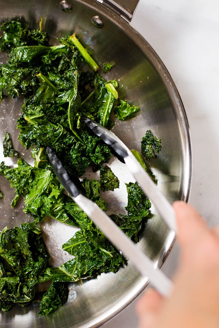 Sauteing kale in a pan on medium heat. Sauteed kale is one of the ingredients used in the Healthy Harvest Buddha Bowl.
