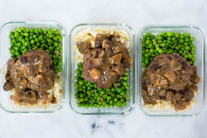 View from the top of 3 meal-prep containers filled with cooked potatoes, peas, Salisbury steak, and Salisbury steak mushroom gravy.