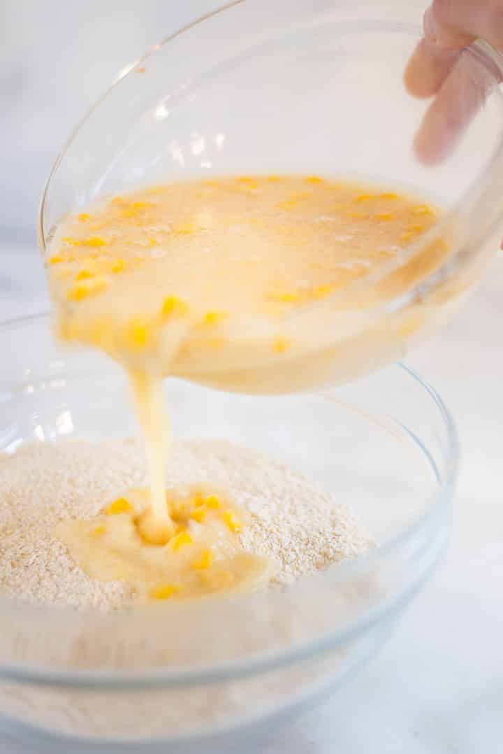 Pouring the wet ingredients (egg, honey, almond milk, coconut oil and corn) for the Easy Sweet Cornbread Recipe over the dry ingredients.