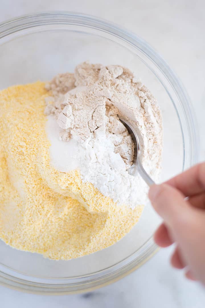 A large mixing bowl filled with the dry ingredients required by the Easy Sweet Cornbread Recipe including spelt flour, cornmeal, baking powder, and sea salt.