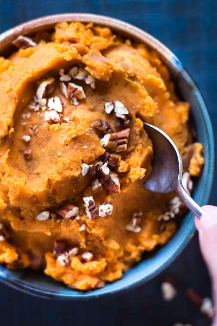 Overhead image of a blue bowl of mashed sweet potatoes, with a hand holding a spoon and dipping into it.