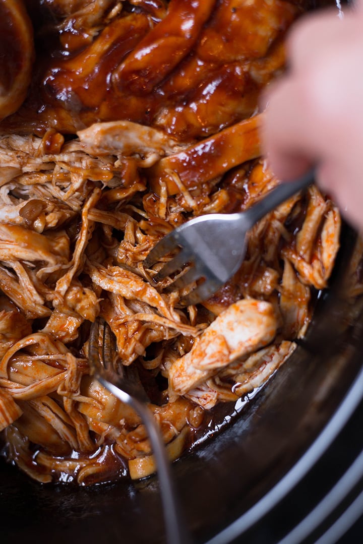 Overhead image of the shredding of slow cooker chicken with 2 forks.
