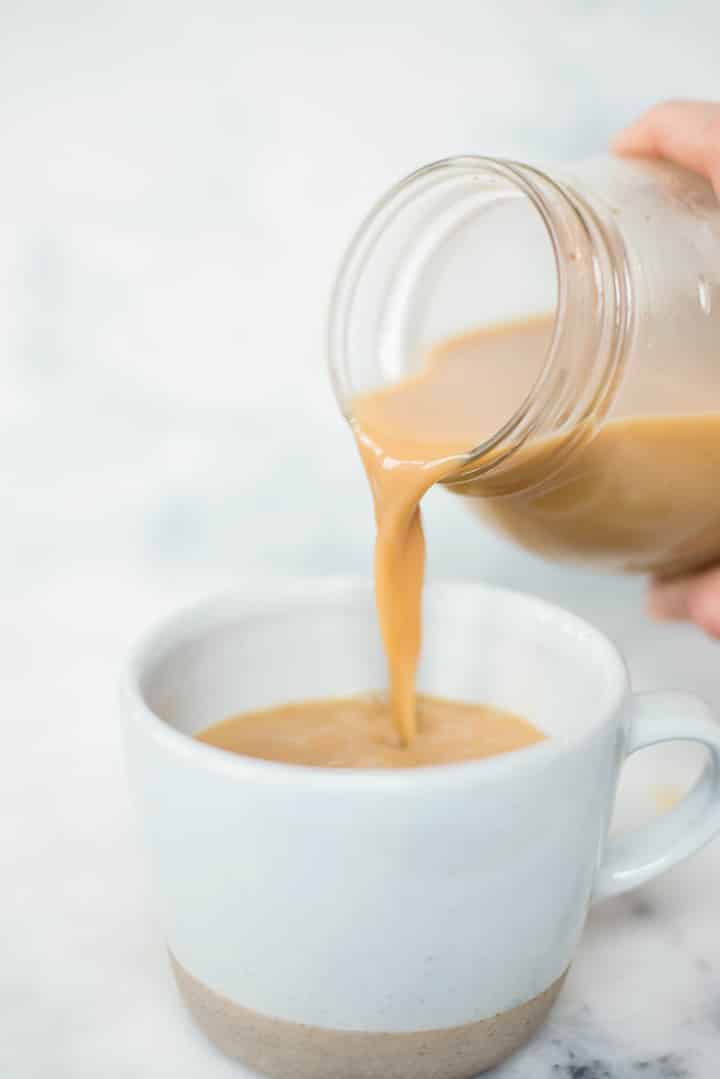 Pouring vanilla latte from a mason jar to a coffee mug.