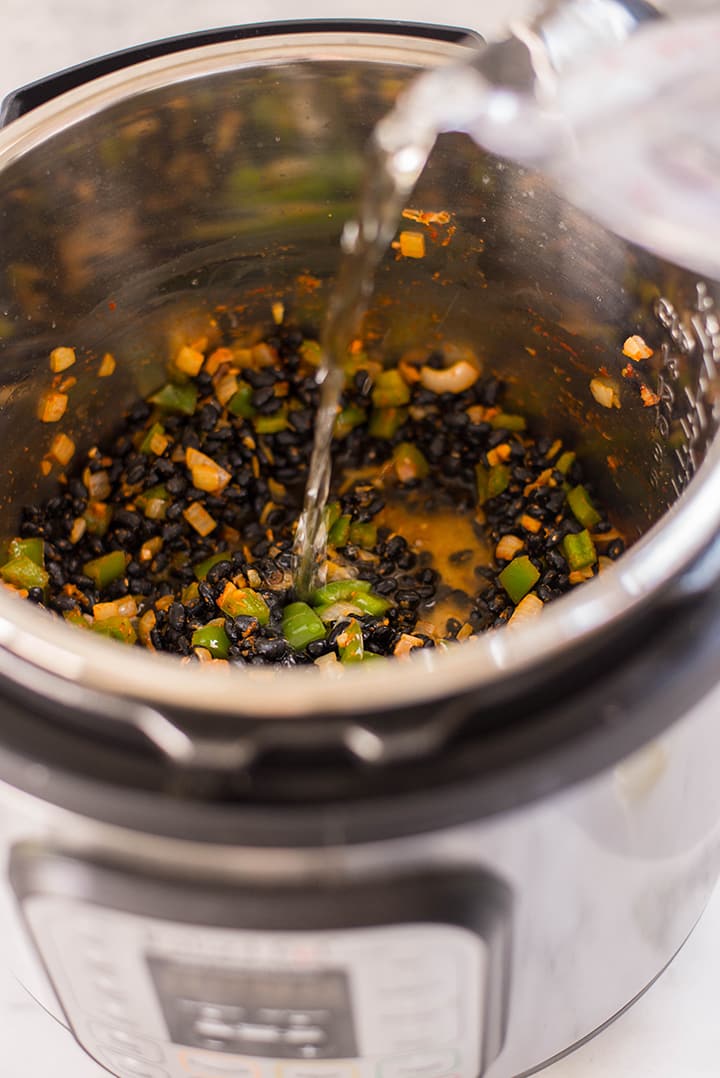 Pouring water over beans, spices, and other ingredients in the instant pot to make Cuban black beans.
