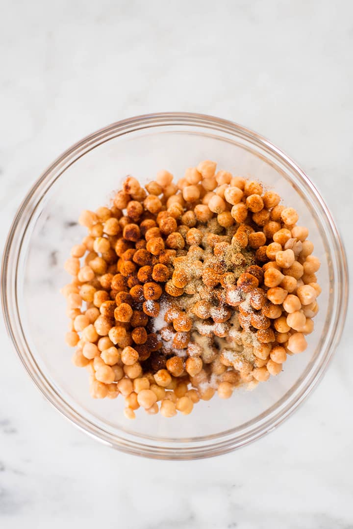 A large bowl filled with chickpeas. Over the chickpeas was added olive oil, chili powder, chipotle chili powder, cumin, sea salt, and garlic powder. 