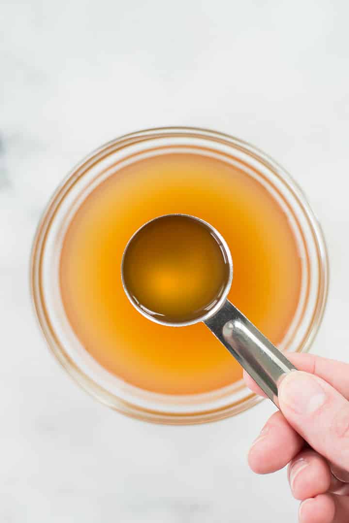 Closeup overhead view of a bowl of apple cider vinegar, with a hand dipping a tablespoon into the bowl.