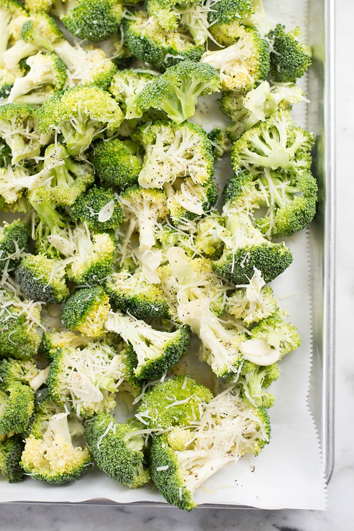 Broccoli florets sprinkled with parmesan and placed on a lined baking sheet.