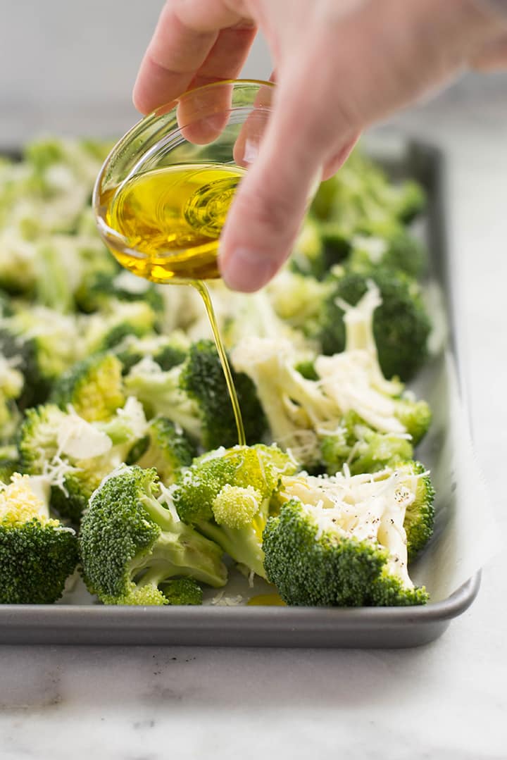 Drizzling olive oil over broccoli florets. The broccoli florets are spread over a baking sheet.