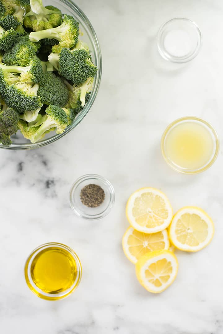 Separate ingredients for lemon roasted broccoli including olive oil, lemon juice & zest, lemon slices, sea salt, pepper.