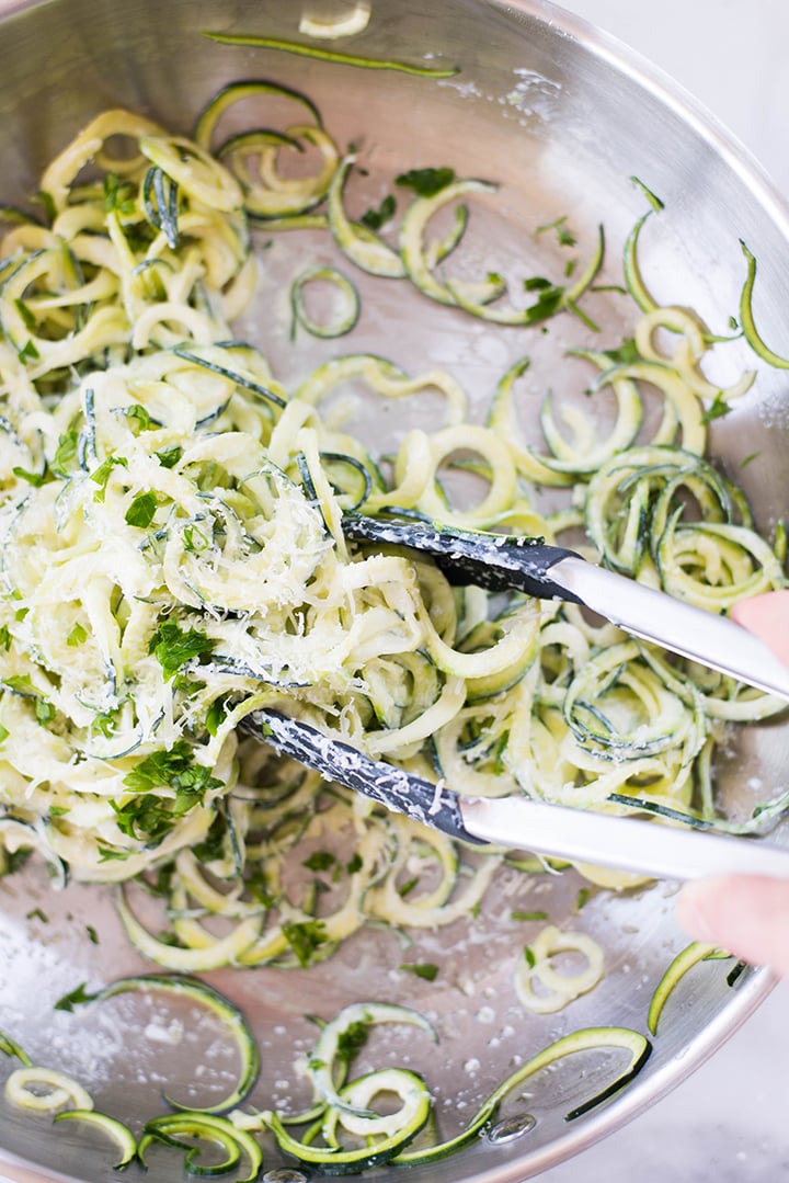 Tossing zucchini noodles with homemade Alfredo sauce and parmesan in a saucepan.