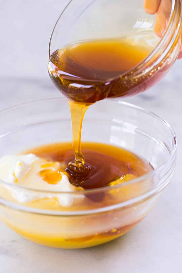 Pouring honey over grek yogurt to make Healthy Honey Mustard Dressing.