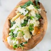 Top view of Spinach And Artichoke Baked Sweet Potato topped with parmesan and chopped parsley.