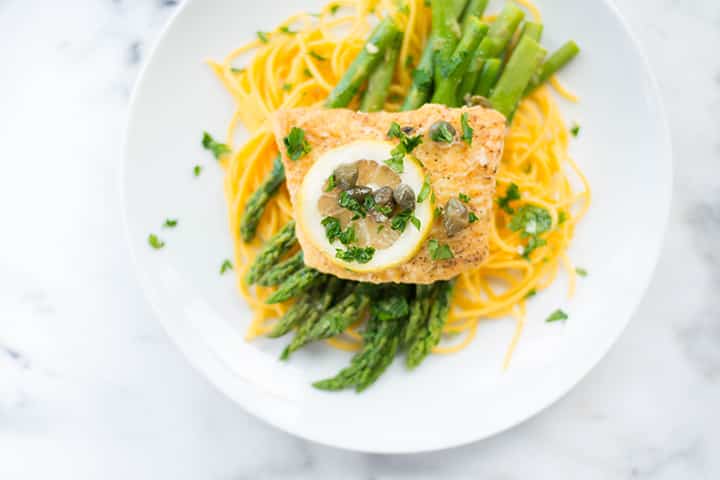 Top view of halibut picatta served over steamed asparagus and chickpea spaghetti.