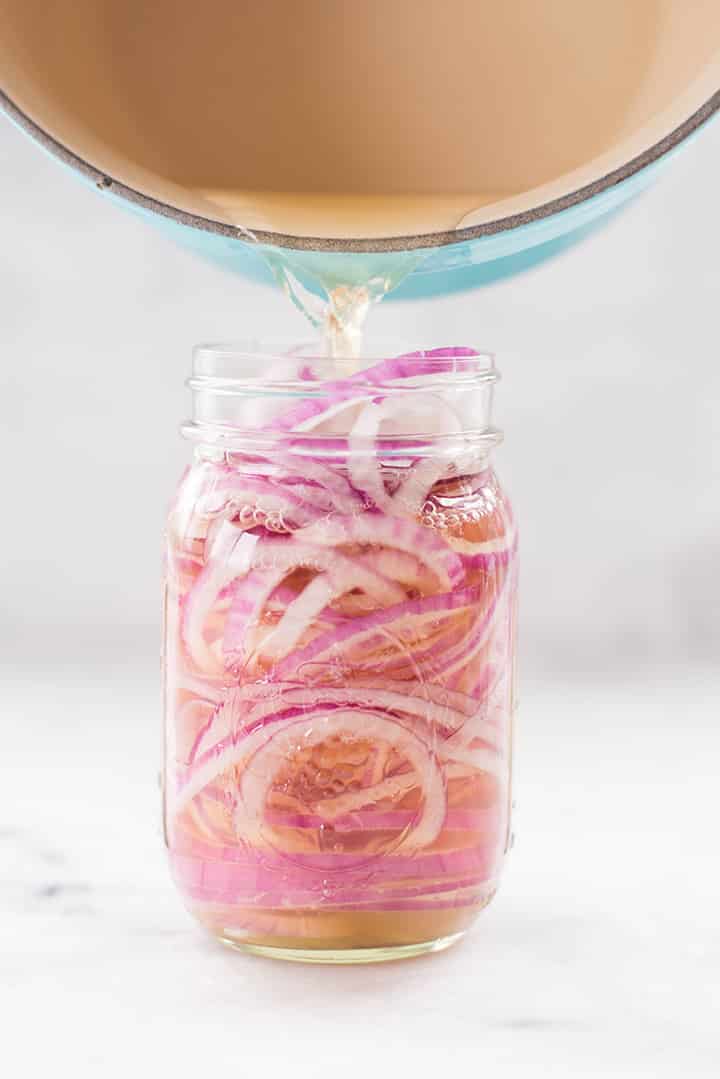 Pouring vinegar mixture over the onion slices in a mason jar.