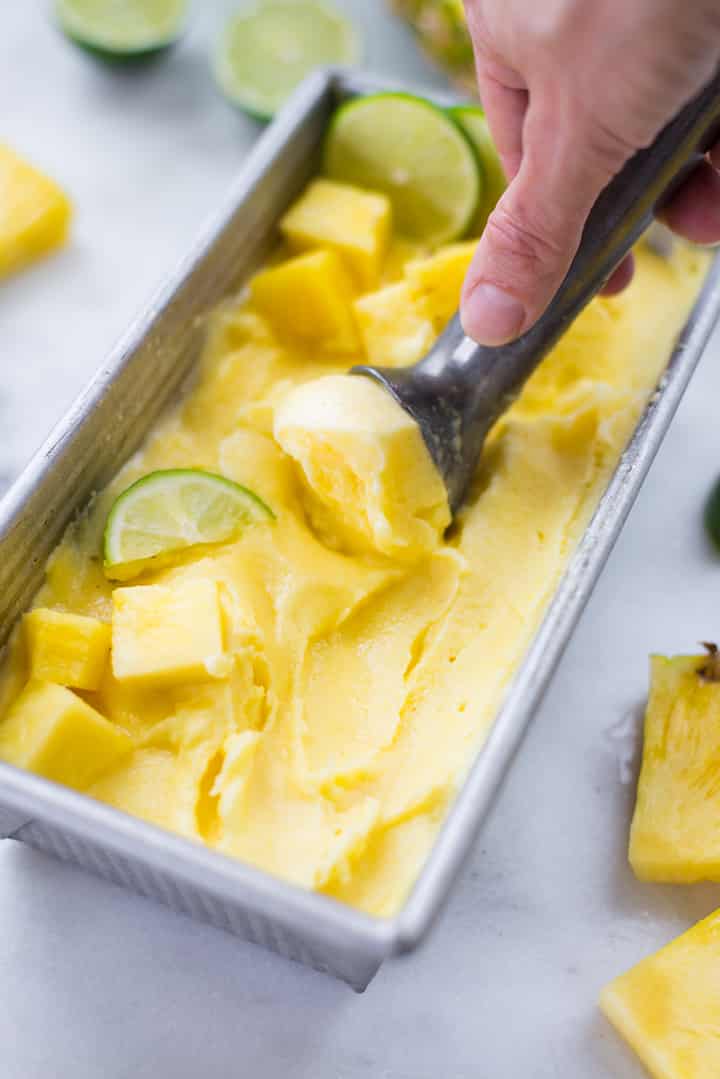 Close up of a loaf pan filled with pineapple sorbet garnished with pineapple cubes and lime slices.