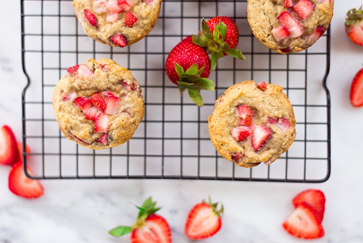 Close up view from the top of 4 strawberry muffins on the cooling rack surrounded by fresh strawberries and fresh strawberries cut in half.