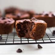 Chocolate muffin with a bite taken out, showing moist texture and melted chocolate chips on a cooling rack.