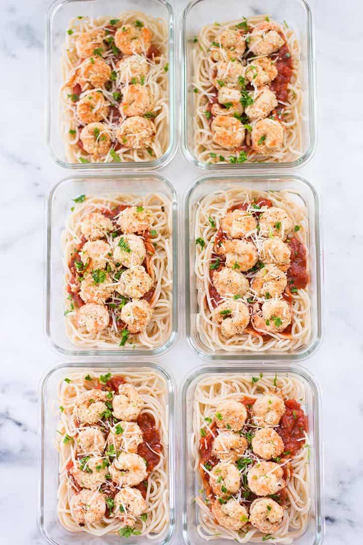 Six glass meal prep containers lined up, filled with breaded shrimp meal prep and brown rice pasta.
