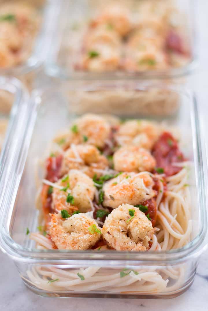 Close-up view of breaded shrimp in meal prep container, can see the crunchy, savory almond meal coating, and the shrimp is topped with parmesan and italian parsley.