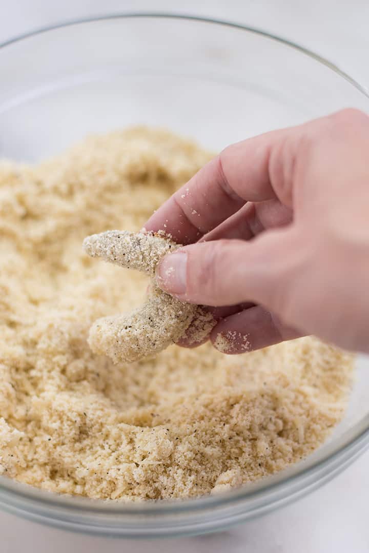 Close-up of hand dredging jumbo shrimp into almond meal coating for healthy breaded shrimp recipe.
