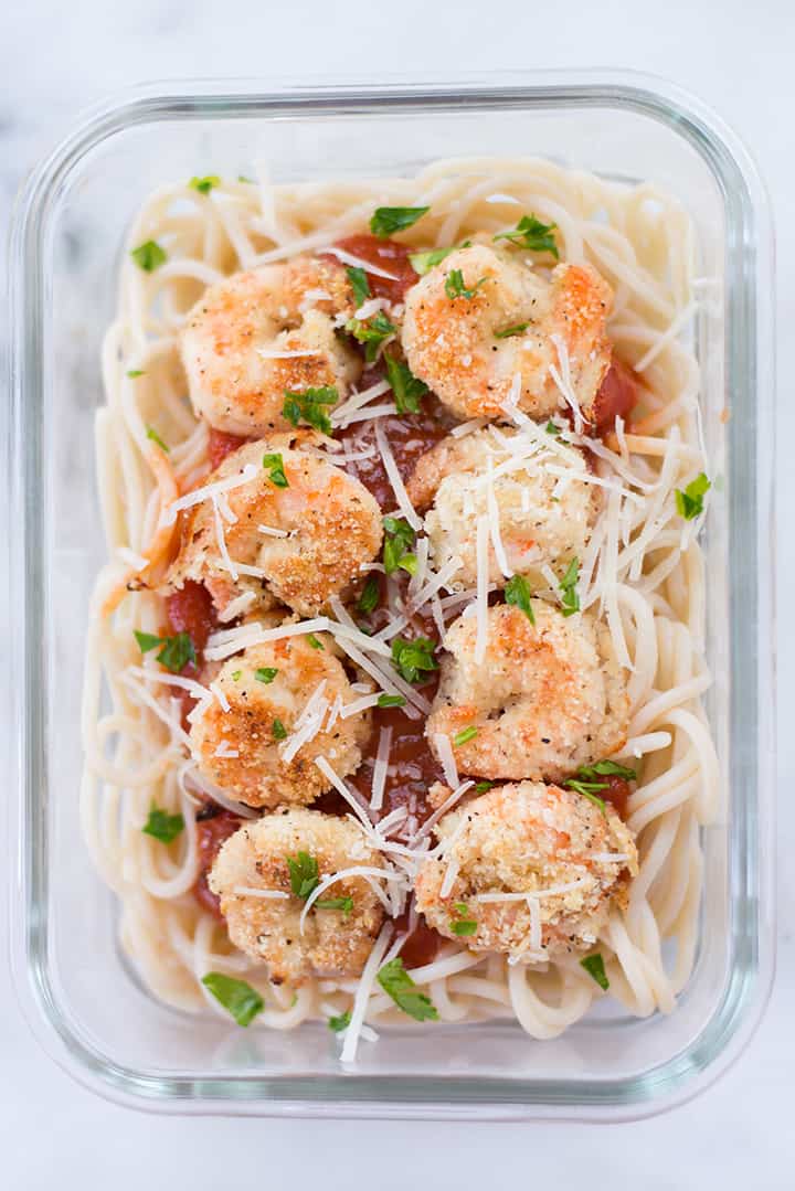 Single glass meal prep container of breaded shrimp meal prep, with breaded shrimp over brown rice pasta and marinara sauce.