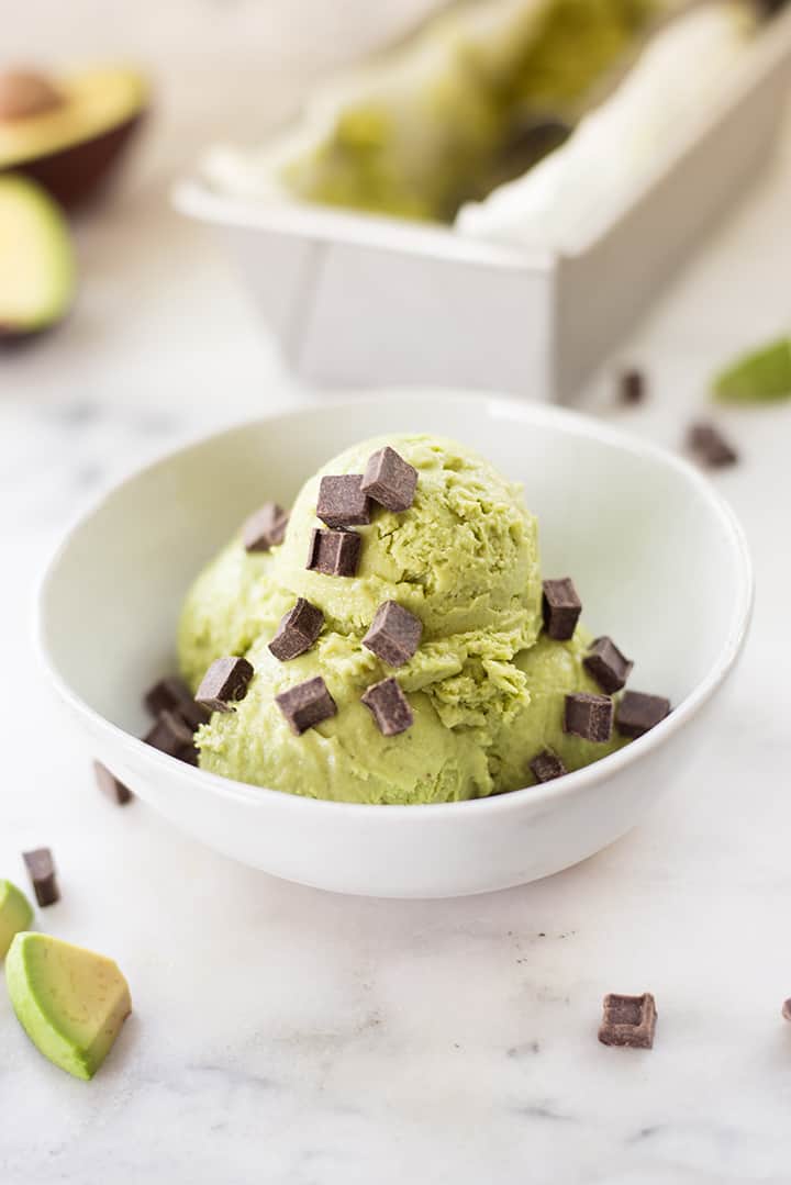 Side view of a bowl filled with three scoops of avocado ice cream, topped with dark chocolate morsels.