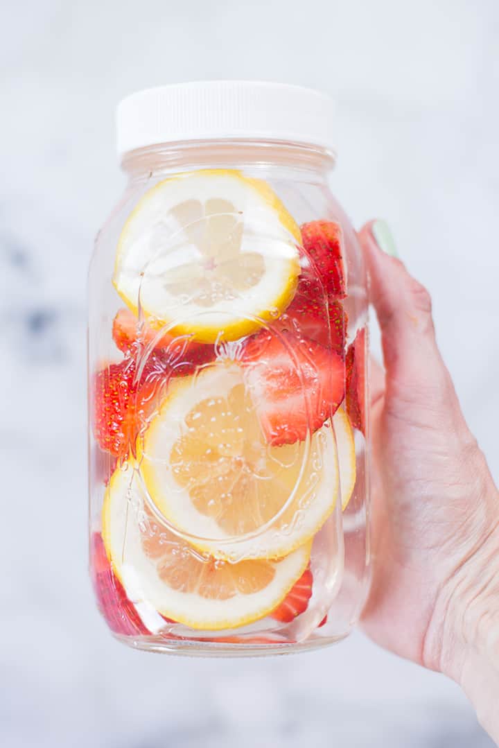 Hand holding strawberry lemon infused water in a 1 quart mason jar and resealable lid.