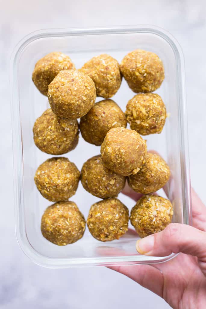 Hand holding meal prep container with the lemon turmeric energy balls which are the snack for the meal plan to reduce inflammation.
