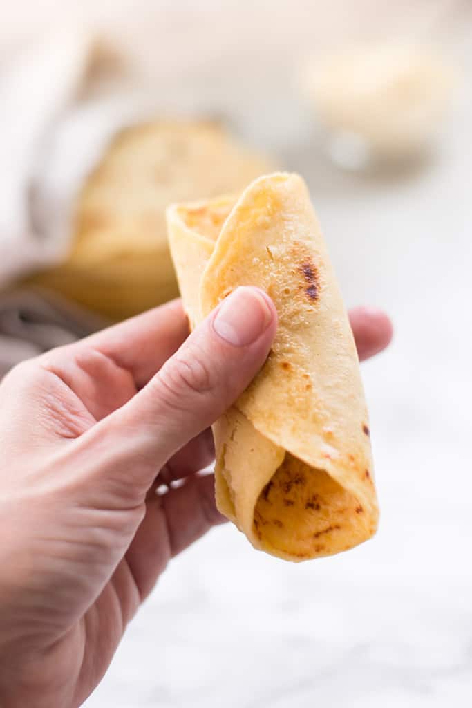 Hand holding a rolled up chickpea flour tortilla to show texture and how flexible the tortilla is.