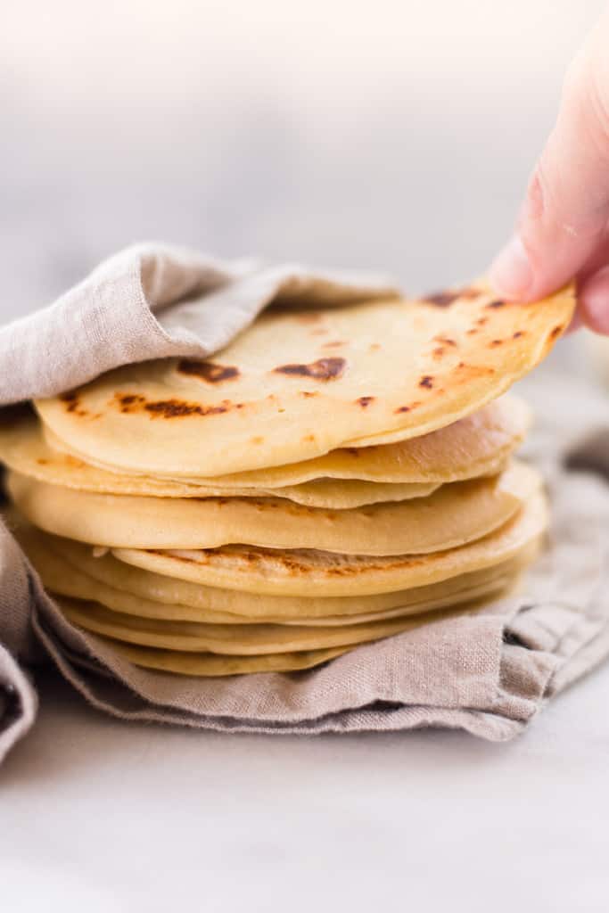 Hand grabbing one chickpea flour tortilla from the top of a stack to show how pliable and flexible the chickpea flour tortillas are.