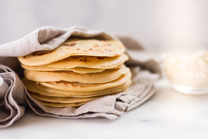 Side view of a stack of several chickpea tortillas that are being kept warn by being wrapped in a kitchen towel.