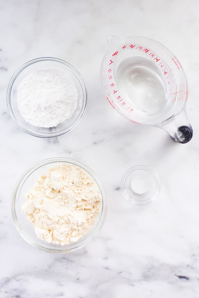 The four ingredients needed for the chickpea tortillas, separated and ready to be added to a bowl, including water, chickpea flour, arrowroot starch, and sea salt.