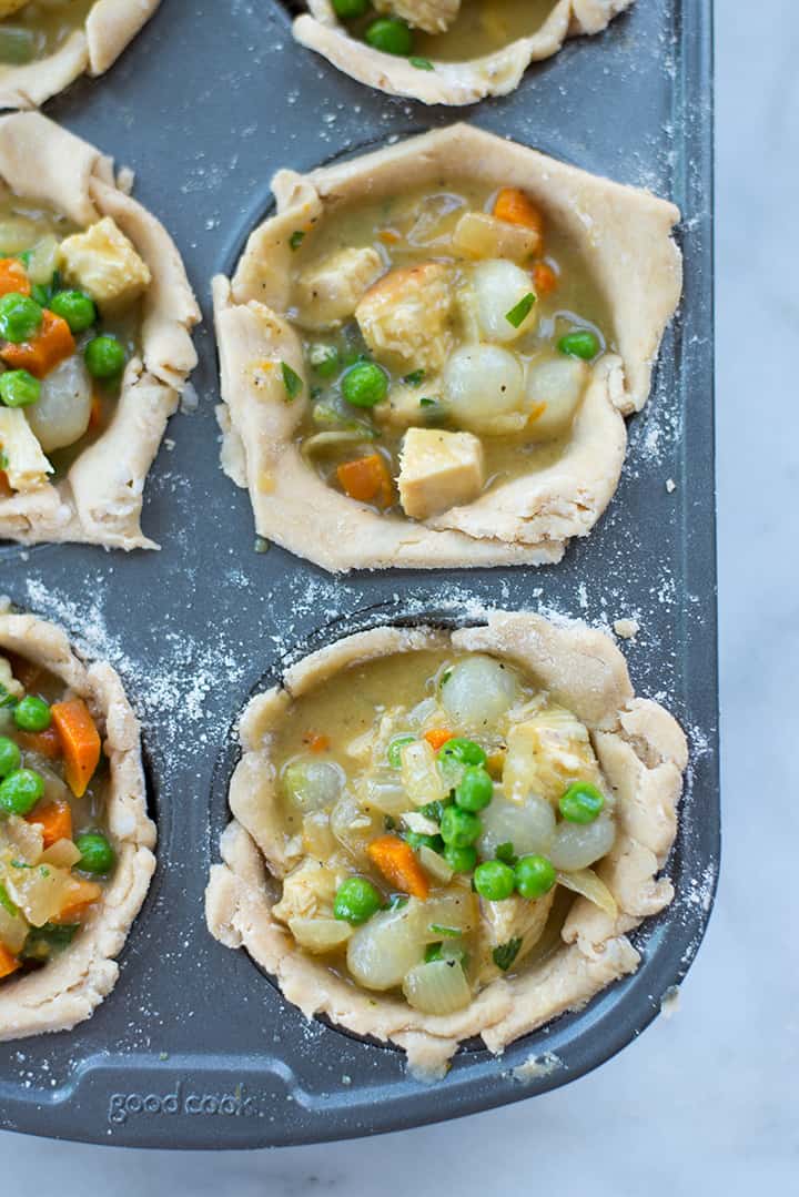 Overhead view of unbaked mini freezer chicken pot pies that have been filled and are ready to be topped with whole wheat pastry crust and then baked.