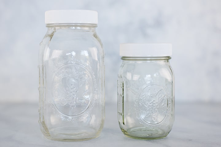 One 1-quart mason jar and one 16-oz mason jar, both empty, with lids, showing different sizes of mason jars to purchase for meal prep containers.