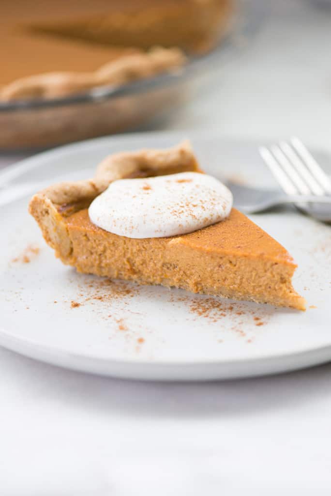 Close up shot of a single slice of pumpkin pie from scratch, topped with fresh vegan whipped cream and cinnamon.
