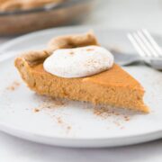 Close up shot of a single slice of pumpkin pie from scratch, topped with fresh vegan whipped cream and cinnamon.
