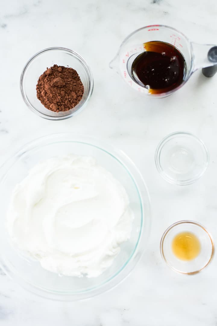 Overhead view of glass bowls holding the ingredients for Healthy Peppermint Bark, including cocoa, pure maple syrup, peppermint extract, Greek yogurt and vanilla extract