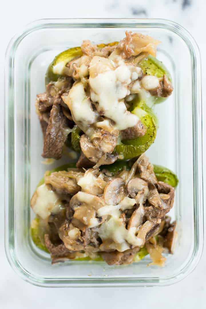 Overhead view of two Philly Cheesesteak Stuffed Peppers in a glass container ready to store as a prepared meal