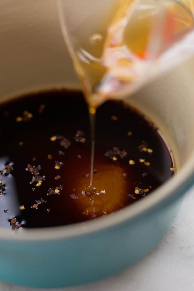 View of raw honey being poured into a sauce pan with ingredients for the best healthy teriyaki sauce, including low sodium soya sauce, fresh ginger, and apple cider vinegar.