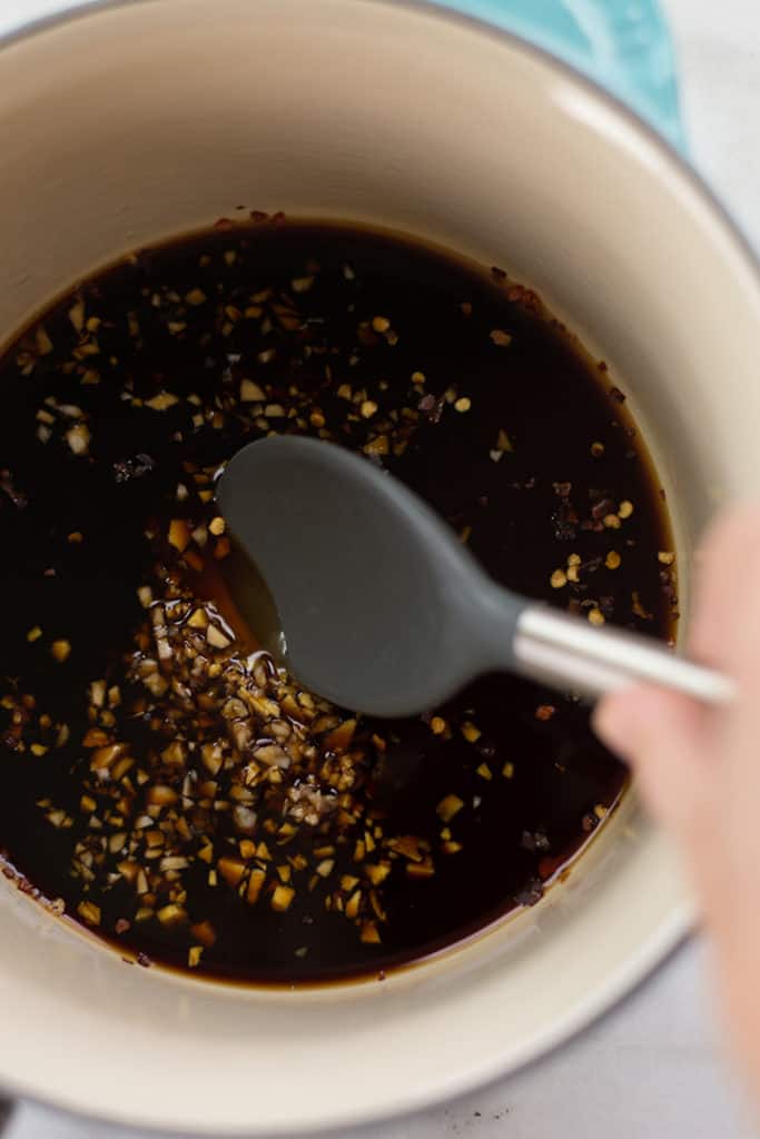 Overhead view of a saucepan of the best healthy teriyaki sauce being stirred as it cooks, with ingredients including fresh ginger, low sodium soya sauce, honey, and arrowroot starch.