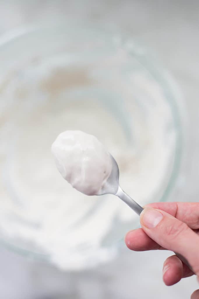 Overhead view of a spoon of 4-ingredient keto whipped cream being scooped out of a glass bowl full of cream.