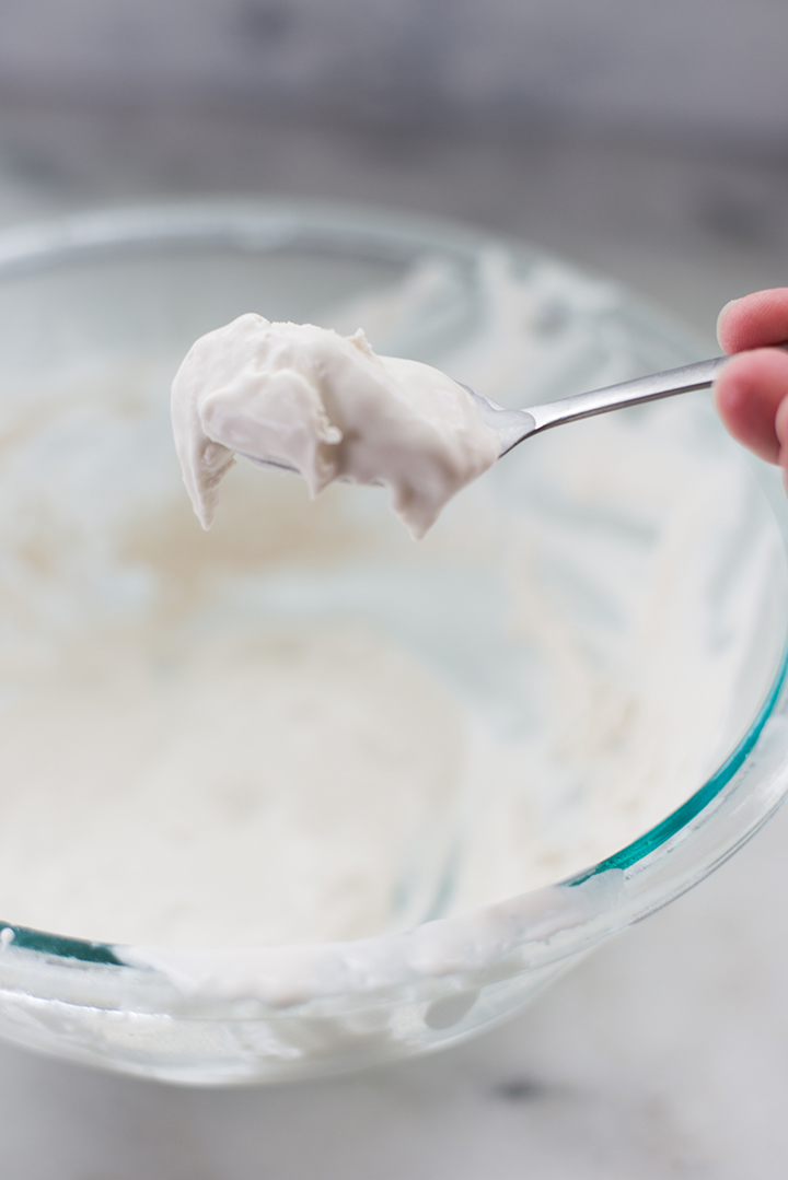 Close up side view of a spoonful of keto whipped cream, being taken out of a glass bowl.