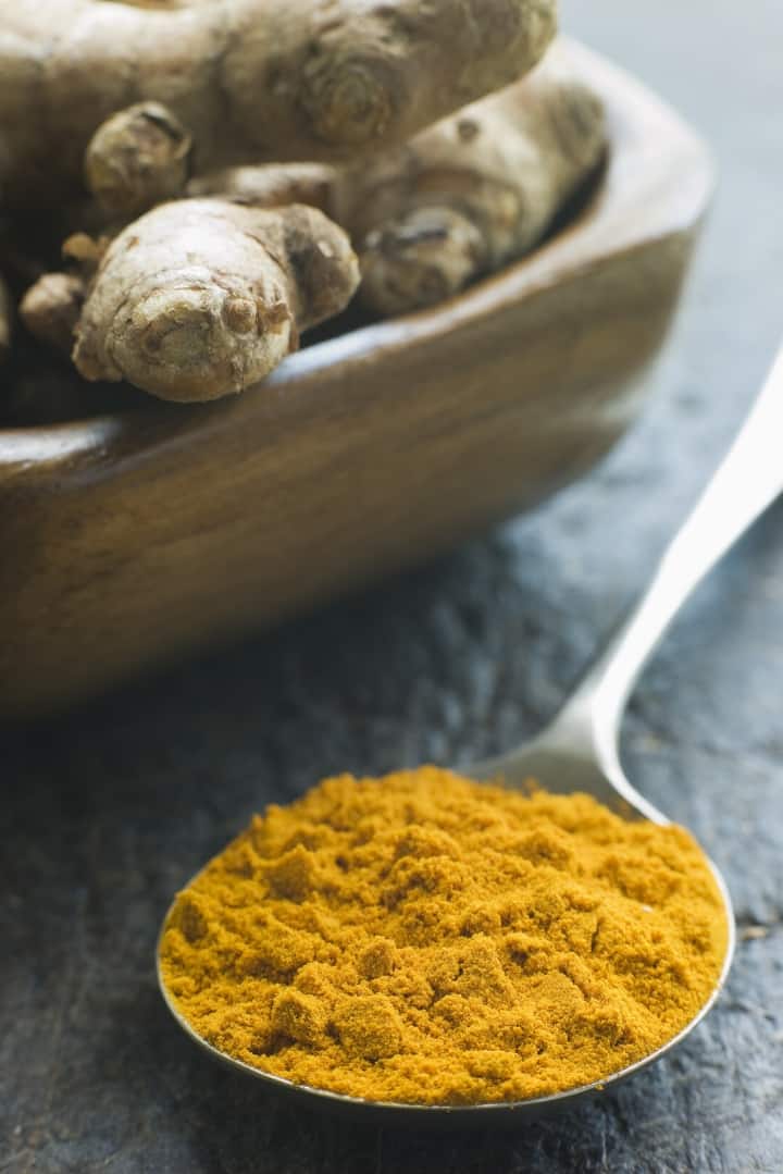 Image of turmeric rhizomes in a wooden bowl and a spoon full of dried turmeric, a spice with many benefits.