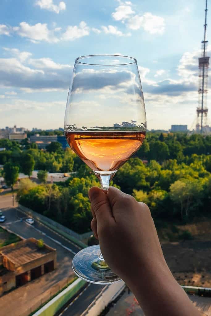 Close up view of a hand holding a glass of wine up in celebration, the background is trees and the street.