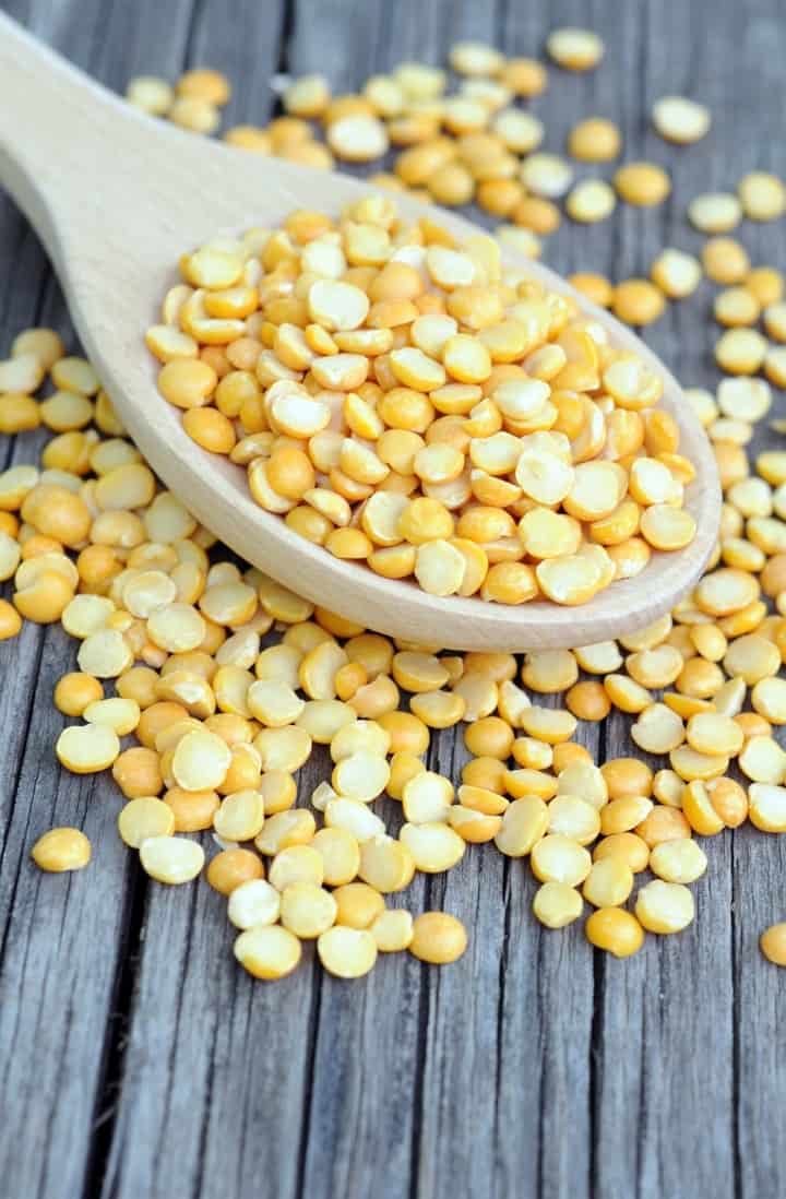 Close up view of a large white spoon full of yellow peas, which are used to make pea protein.