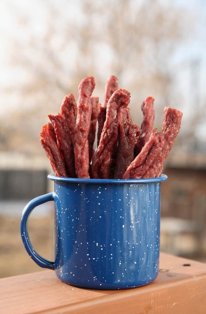 Close up side view of a blue tin cup filled with strips of beef jerky.