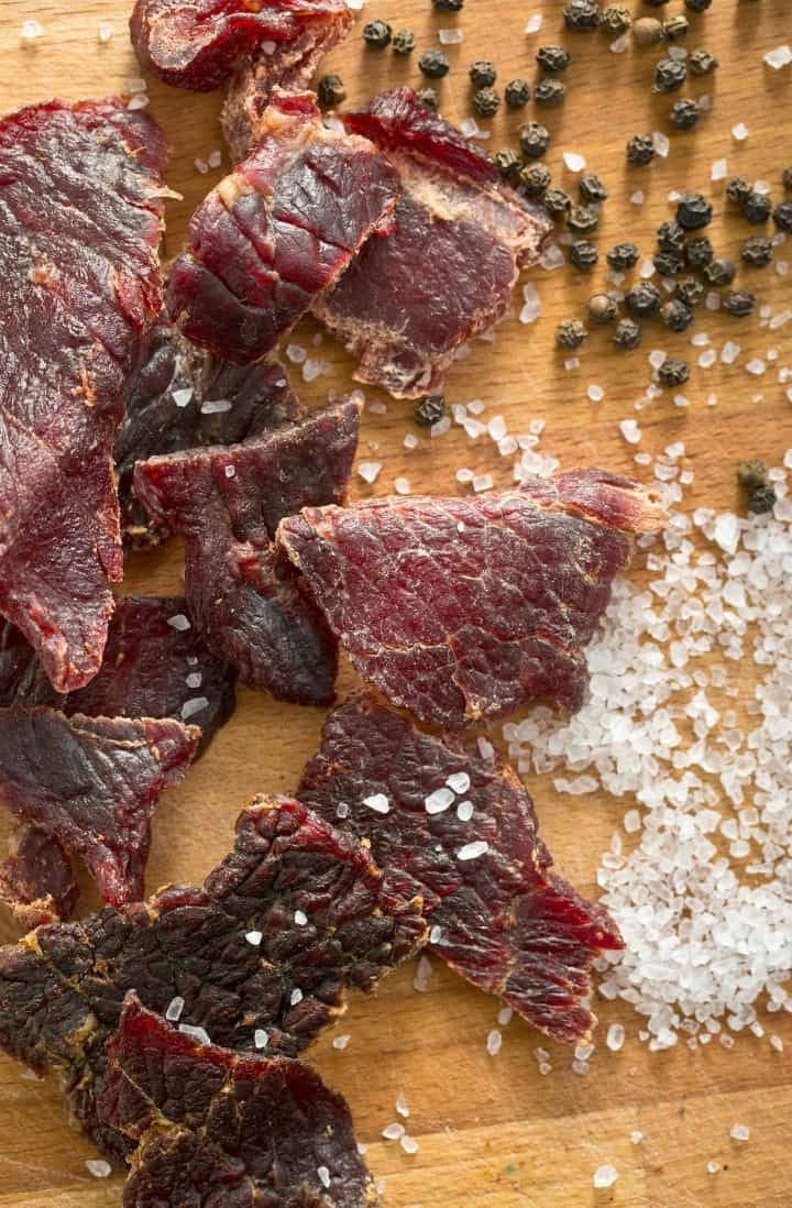 Overhead image of some pieces of prepared beef jerky, with spices surrounding it.