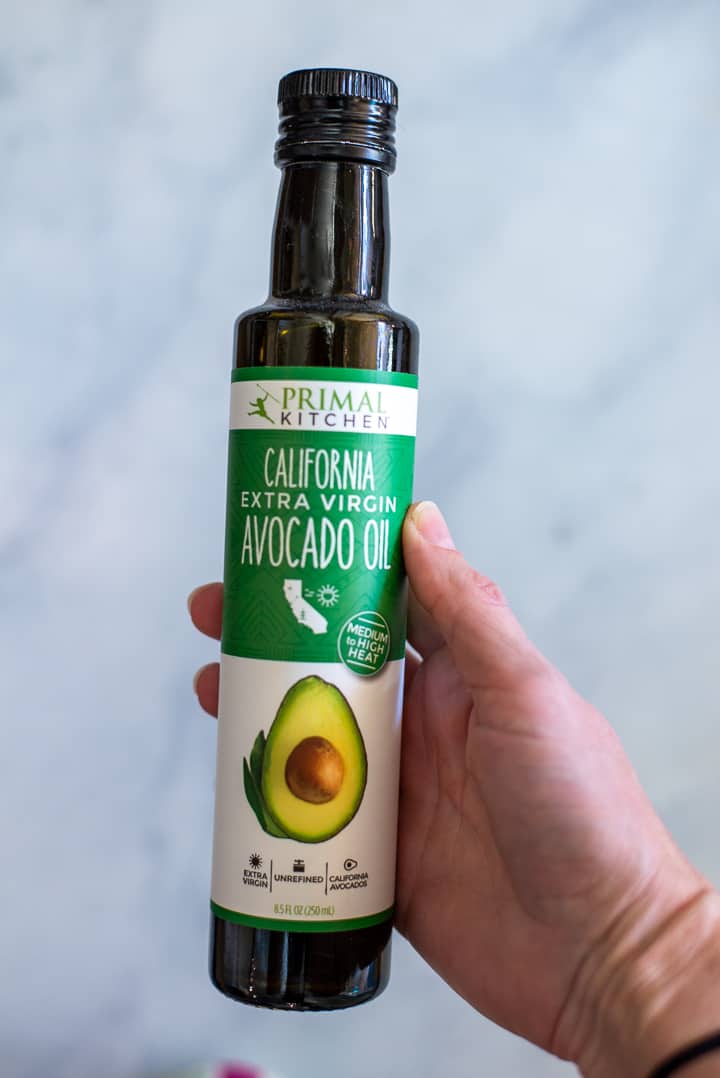 Close up image of a hand holding a glass bottle filled with California Avocado Oil.
